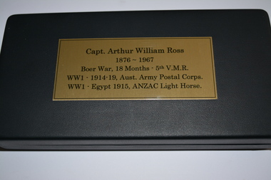 Medals contained in black covered box with gold coloured metal  plaque with black printing attached to lid.