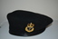 Black wool beret with black vinyl band.  At front two eyelets affixed with gold coloured metal badge consisting of an anchor below a crown.