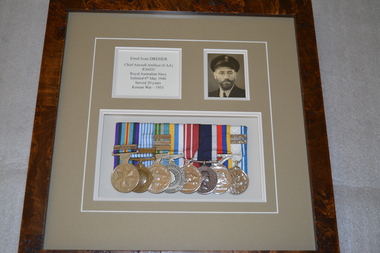 Brown frame containing beige mount housing black and white photograph and set of 8 medals