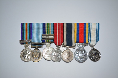 Set of seven miniature metal medals with multi coloured stripped ribbons attached.  All mounted on a large metal pin attached at rear.