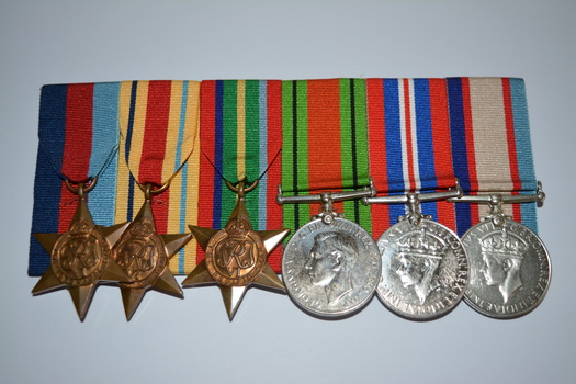 Six medals with multi coloured ribbons attached mounted on black felt with large pin attached at rear.  