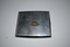 Square silver metal case with left side hinge. A small rising sun badge is affixed in centre on top cover.