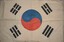 Large rectangular calico cloth with blue and red circle in centre and four groups of three short black lines in each corner. String attached to top and bottom left edge.