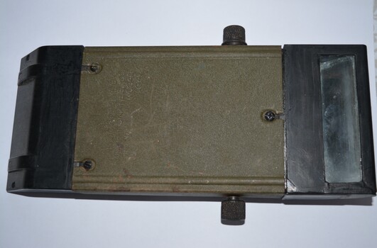 Rectangular shaped black and green metal object with sloping ends containing glass. Black metal handle at front with small black knobs attached to both sides.