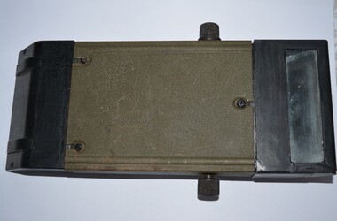 Rectangular shaped black and green metal object with sloping ends containing glass. Black metal handle at front with small black knobs attached to both sides.