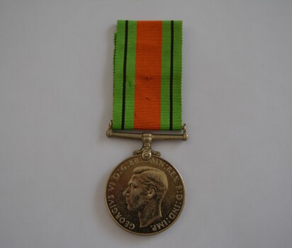 Round silver metal medal with green orange and black striped ribbon attached