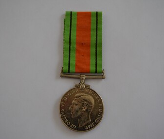 Round silver metal medal with green orange and black striped ribbon attached