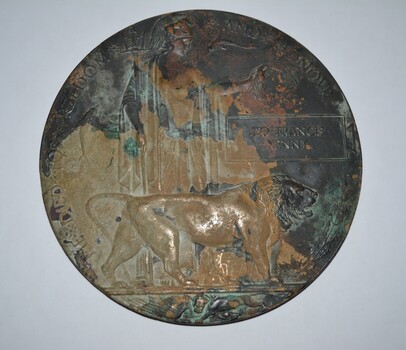 Round bronze plaque includes an image of Britannia holding a trident and standing with a lion with name of deceased soldier on right side.