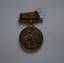 Round silver metal medal with remnants of blue and orange ribbon on attached clasp suspender bar. 
