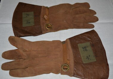 Brown suede gloves with brown ribbon strap threaded through an eyelet and secured with a press stud.  