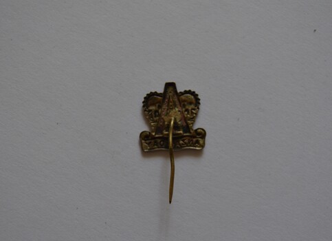 White metal crown shaped with capital A above scroll lapel badge with pin attached 