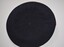Dark blue felt beret with black leather trim with enclosed ribbon with white metal badge of coat of arms attached to red felt square handsewn at front.