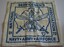 Square shaped cushion cover in cream cotton material with emblem stamped in blue and three buttons on rear side