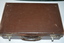Brown leather briefcase with handle attached.  There are two metal clips on lid with locking devices attached to base.  There are metal corners attached to edges of lid.