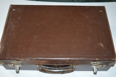 Brown leather briefcase with handle attached.  There are two metal clips on lid with locking devices attached to base.  There are metal corners attached to edges of lid.