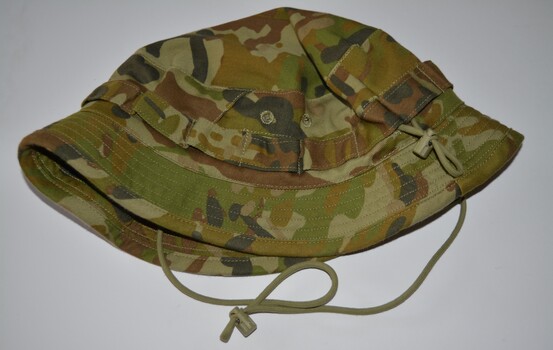 Camouflage fabric hat with short wide brim with loops stitched around band with draw string attached.