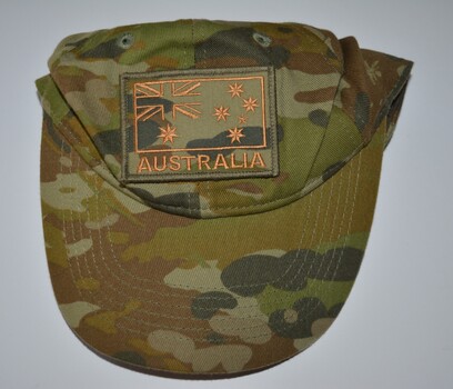 Camouflage fabric cap with vent holes, detachable badge above peaked brim.