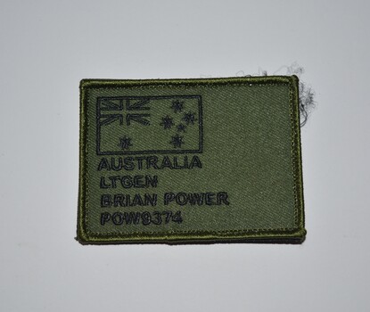 Oblong shaped green fabric name tag with black stitching attached to Velcro.