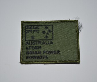 Oblong shaped green fabric name tag with black stitching attached to Velcro.