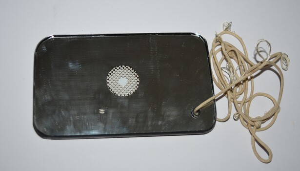 Oblong shaped mirror with circular cross hatched section in the centre.  Is housed in black half case with red writing. Long cord attached through hole in mirror.