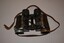 Black painted metal binoculars originally covered in black leather with little remaining.  The brown leather strap is well worn and missing stud fixing on right side.
