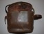 Brown leather look binocular case lined in brown colour cloth.  Long narrow leather strap fixed along sides by leather secured in place by metal studs.  Fitted lid is attached by leather strap fixed in place by four metal studs at rear.  At front is a spring closing mechanism which is broken.