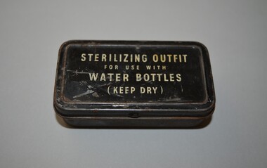 Rectangular tin with hinged lid containing two clear glass vials of water sterilization tablets. The tin is plain metal apart from the black lid with white lettering.  The two vials are stoppered  with cork. 