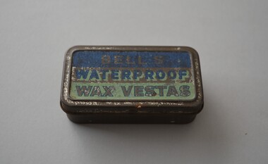 Rectangular tin with hinged lid containing small timber matches with wax heads. The tin is plain metal apart from two tone blue lid with lettering.   Underneath is a serrated patch used to strike the match.