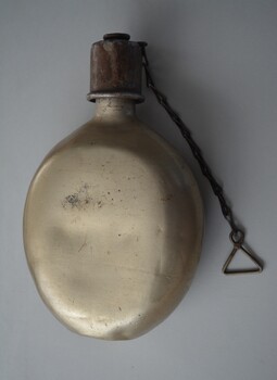 Unpainted aluminium oval shaped water canteen with brownish screw top lip with chain attached.