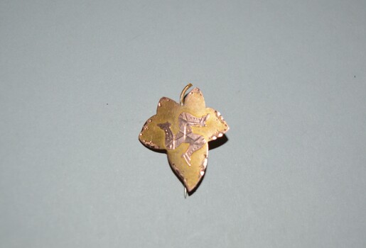 Small leaf shaped gold brooch with three leg symbol or Triskelion in the centre with hinged pin attached at rear.