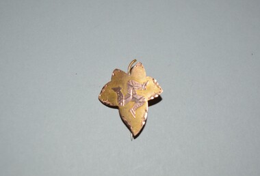 Small leaf shaped gold brooch with three leg symbol or Triskelion in the centre with hinged pin attached at rear.