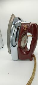 Steam iron standing on its end, showing the Hoover logo on the cranberry-coloured Bakelite handle.