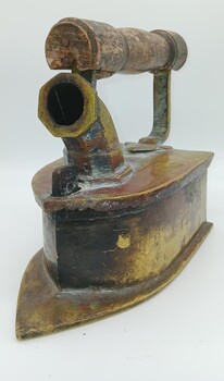 Brass charcoal iron from the front, showing pointed base, charcoal container and chimney. At the top, over the chimney is the wooden handle.