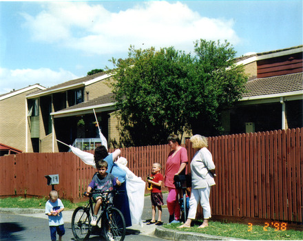 A group of women and children talking by the side of the road. One boy on a bicycle.