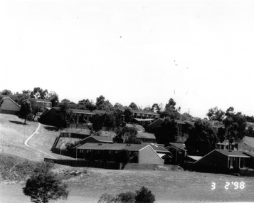 Black and white image of double storey brick houses on a hill side.