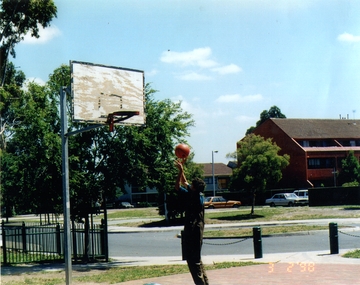 A young man, centre, throwing a basket ball at the hoop, left, with double storey houses in the background.