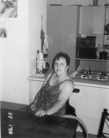 A woman in a wheelchair sitting at her kitchen table.