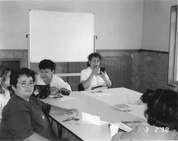 Women sitting around a table, one, front left with glasses, is looking at the camera.