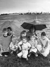 A group of children in a paddock, one is holding an umbrella