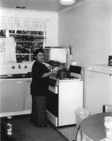 A woman stands, centre, at a stove cooking.