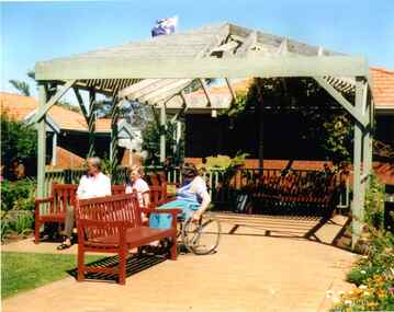 Three people in the sun under a pergola.