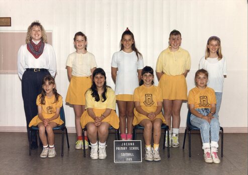 Two rows of students dressed in yellow and white; an adult is standing on the left in the back row