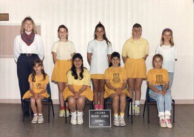 Two rows of students dressed in yellow and white; an adult is standing on the left in the back row