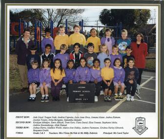 A group of children standing in three rows with teachers either side smiling at the camera with playground visible in background. 