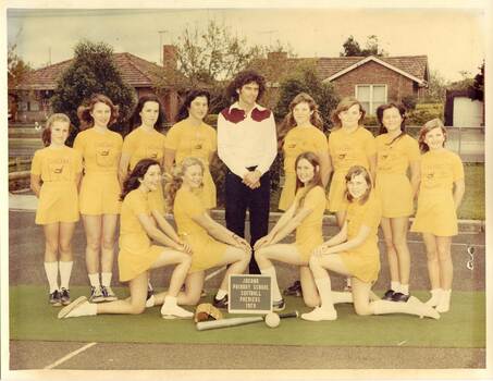 Two rows of girls dressed in yellow with teacher in the back centre wearing a white shirt with burgundy yoke.