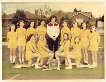 Two rows of girls dressed in yellow with teacher in the back centre wearing a white shirt with burgundy yoke.