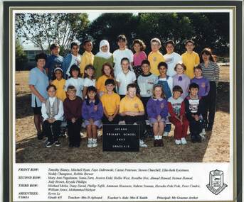Three rows of children with their teachers standing outside in the playground smiling for the camera.