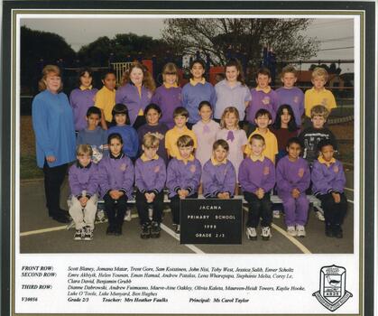  Students, in 3 rows, in school uniform, their teacher is on the left-hand side, the school playground visible in background.