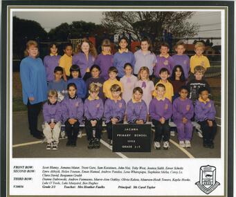  Students, in 3 rows, in school uniform, their teacher is on the left-hand side, the school playground visible in background.