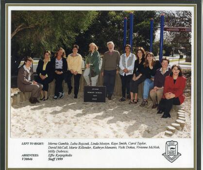 Adults sitting in one row on wooden structure, the school playground visible in background.